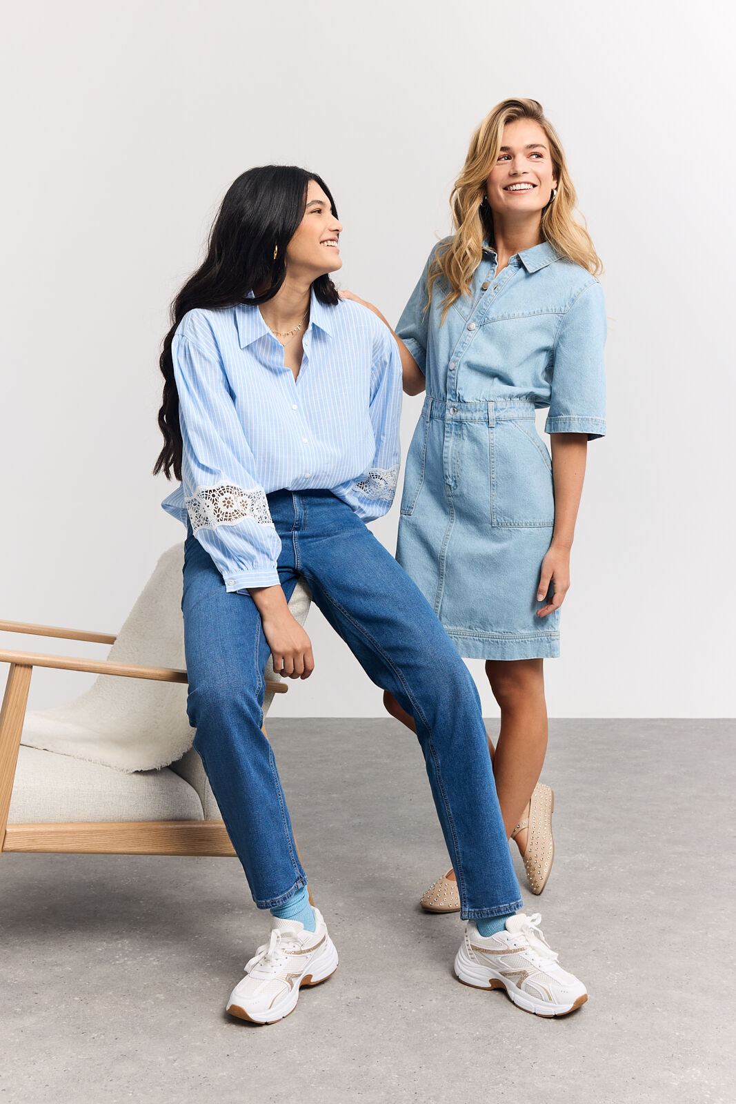 1 woman sitting on the edge of a chair smiling to another woman who is standing besides her